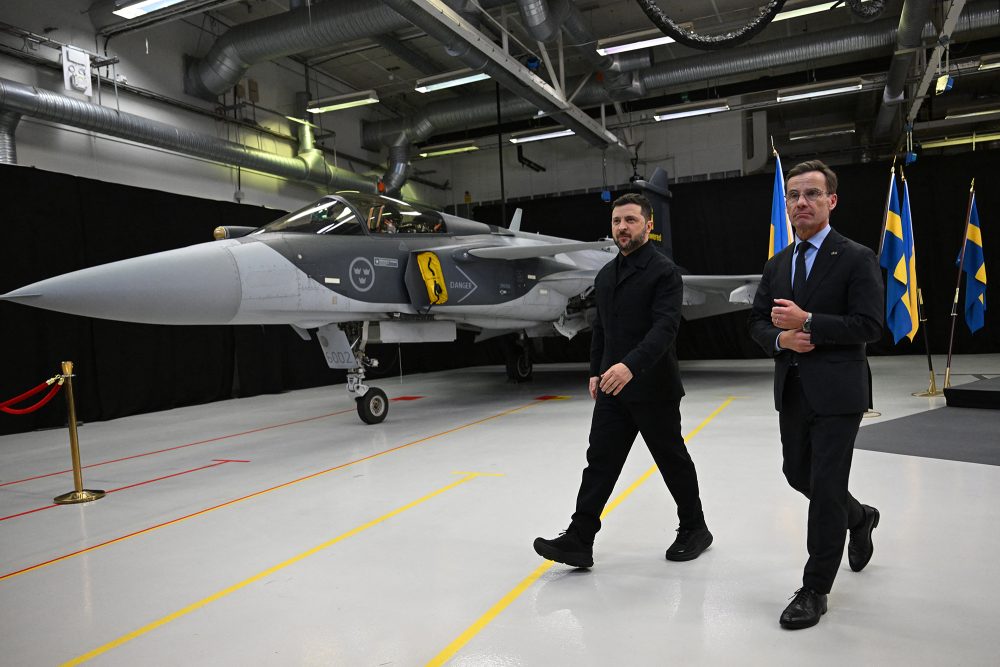 Der schwedische Ministerpräsident Ulf Kristersson und der ukrainische Präsident Wolodymyr Selenskyj gehen an einem der in einer Halle geparkten Kampfflugzeuge vorbei