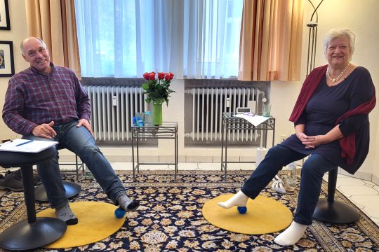 Patient Bernhard Huppertz mit Therapeutin Maria Holl - beide rollen ihre Füße auf einem Ball ab