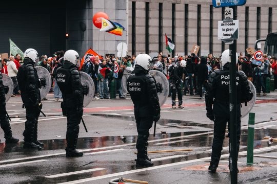 Demonstranten mit Fahnen und Polizisten mit Helmen, Schlagstöcken und Schilden vor einem Tunnel in Brüssel