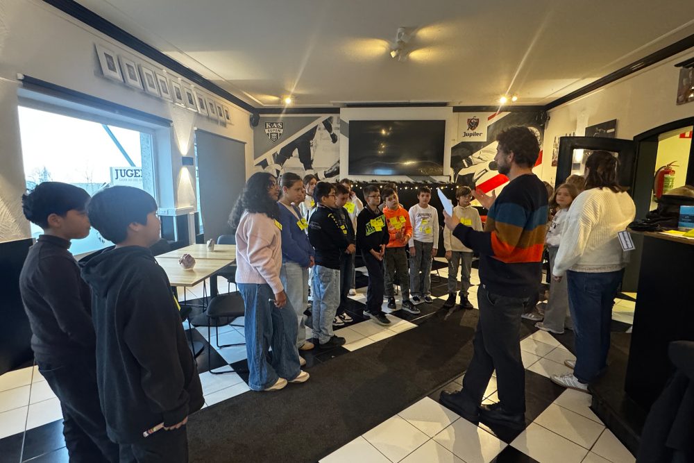 Kinder stehen im Kreis um den Workshop-Leiter herum udn hören ihm zu