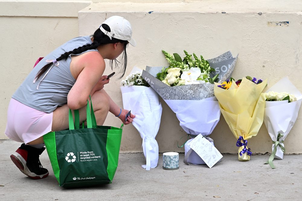 Trauernde Frau legt Blumen an einer Mauer ab
