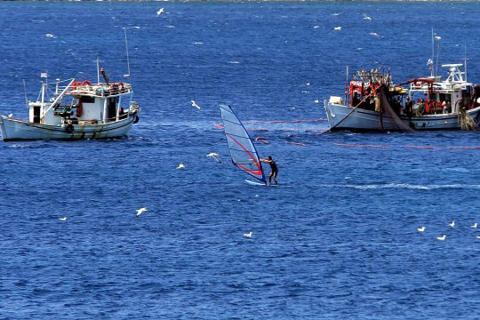 zwei Fischerboote, ein Windsurfer auf dem Wasser
