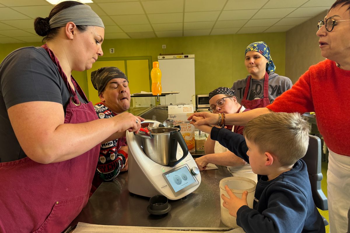 Ein Junge kippt Mehl in eine Küchenmaschine, um ihn herum sind Betreuer und Mitarbeiter des Hof Peters