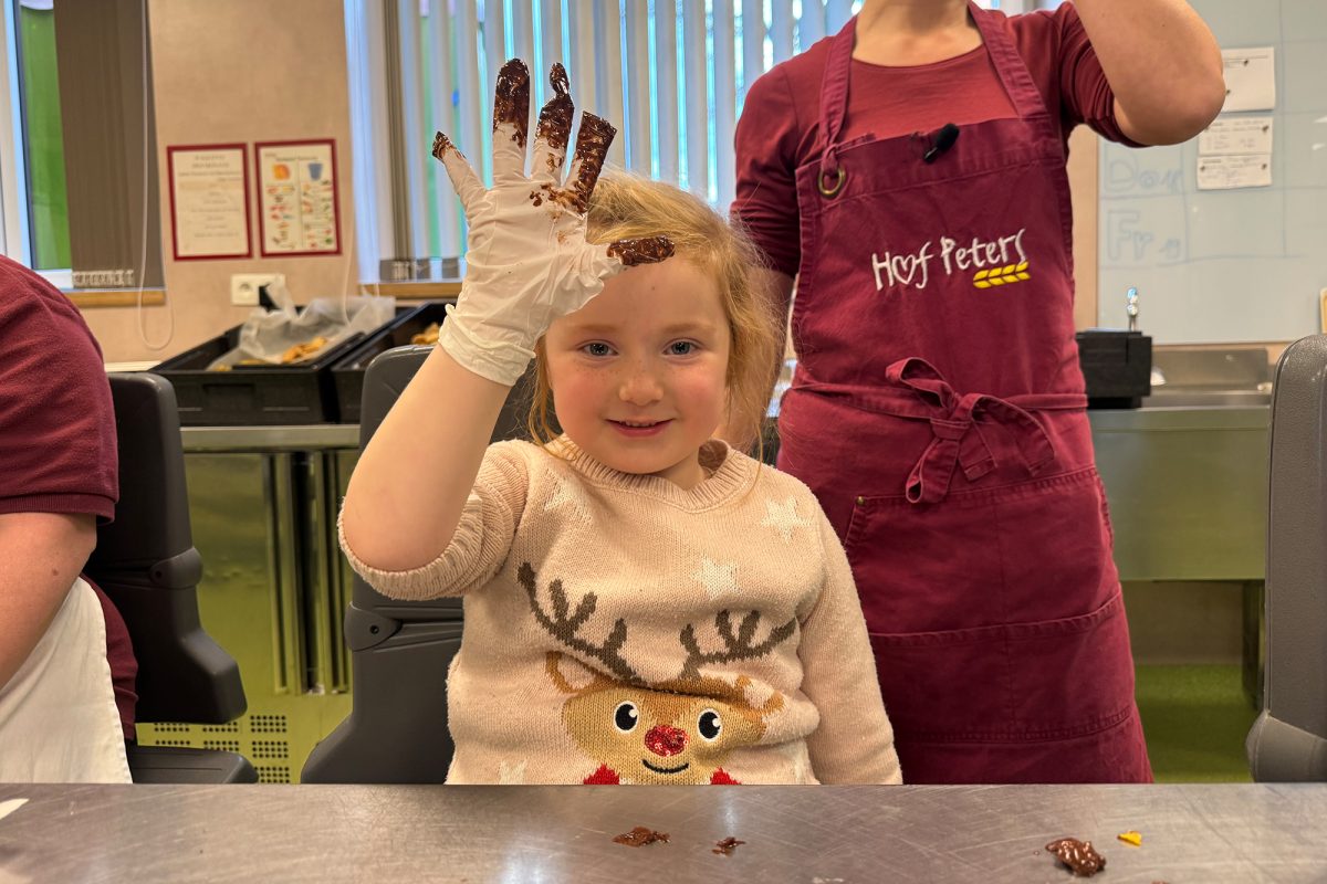 Mädchen hält ihre Hand in die Höhe, an ihrem Küchenhandschuh klebt viel Schokolade