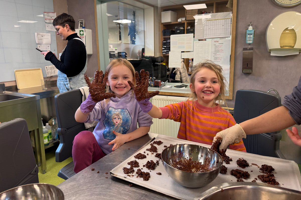 Zwei Kinder halten je eine Hand in die Höhe, an der sie einen schokoladenverschmierten Handschuh tragen