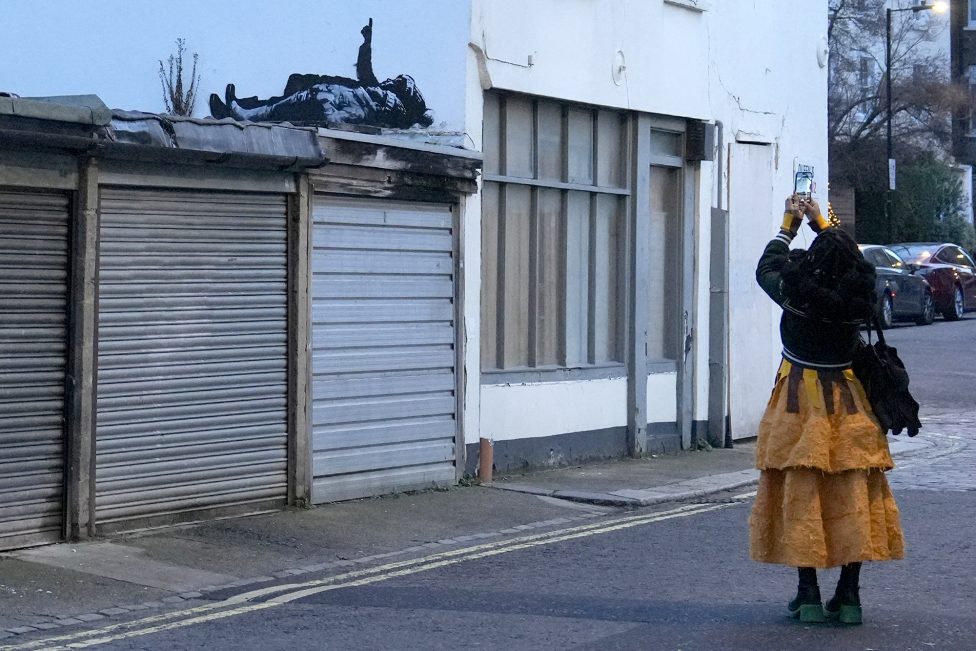 Eine Frau fotografiert das Banksy-Graffiti an der Häuserwand über ihr