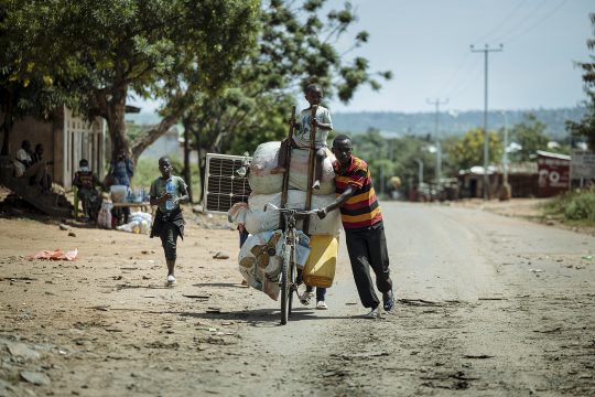 Einwohner fliehen vor den Kämpfen, Mann schiebt hoch beladenes Fahrrad, Kind läuft daneben
