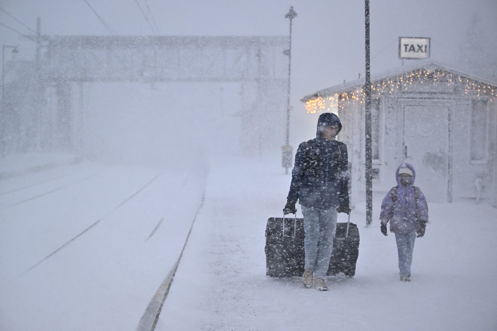 eine Frau und ein Kind ziehen ihre Koffer durch den wirbelnden Schnee