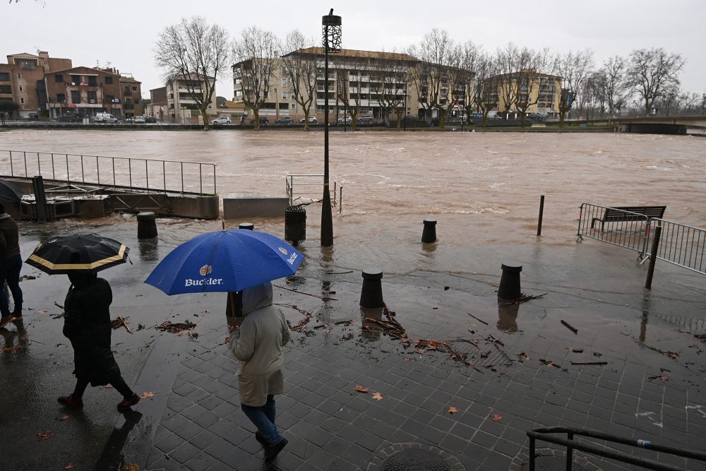 Passanten mit Schirmen schauen auf das Hochwasser