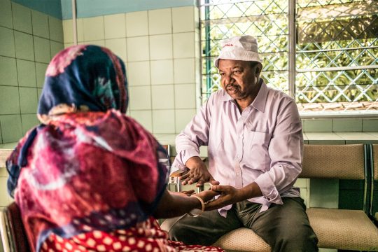 Ambulanz in einem Entwicklungsland: ein Mann spricht mit einer Frau, die ihm ihre Handflächen zeigt