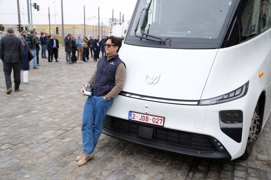 Windrose-Chef Wen Han lehnt an einem seiner LKW und hält ein LKW-Modell in der Hand
