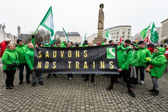 Streikende Bahnbeschäftigte vor dem Brüsseler Zentralbahnhof halten ein Transparent hoch mit der Aufschrift, auf Deutsch übersetzt, "Rettet unsere Züge"