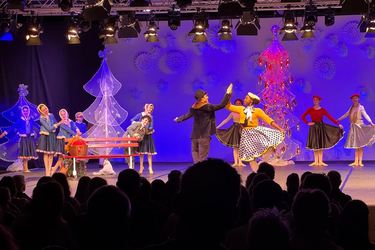 Balletttänzer auf der Bühne während der Aufführung, vorne im Bild die Umrisse des Publikums von hinten