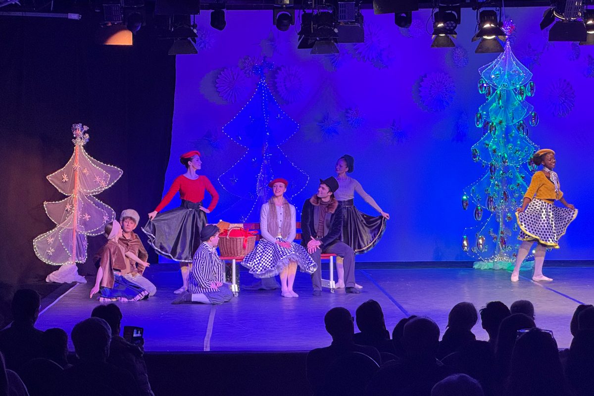 Balletttänzer auf der Bühne während der Aufführung, vorne im Bild die Umrisse des Publikums von hinten