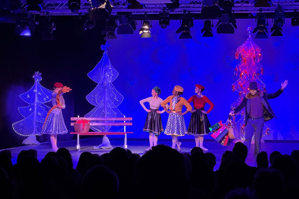 Balletttänzer auf der Bühne während der Aufführung, vorne im Bild die Umrisse des Publikums von hinten