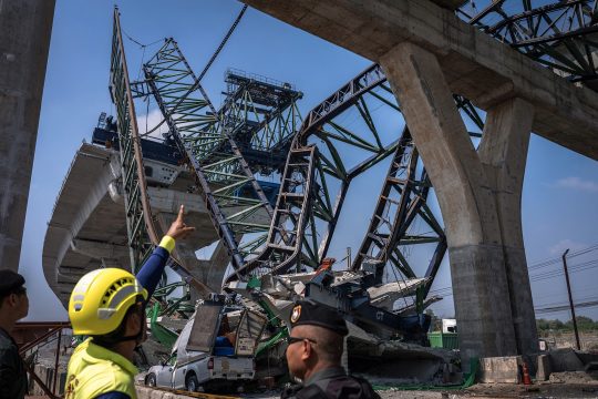Zwei Rettungskräfte schauen auf den umgestürzten Baukran an der Autobahnbrücke