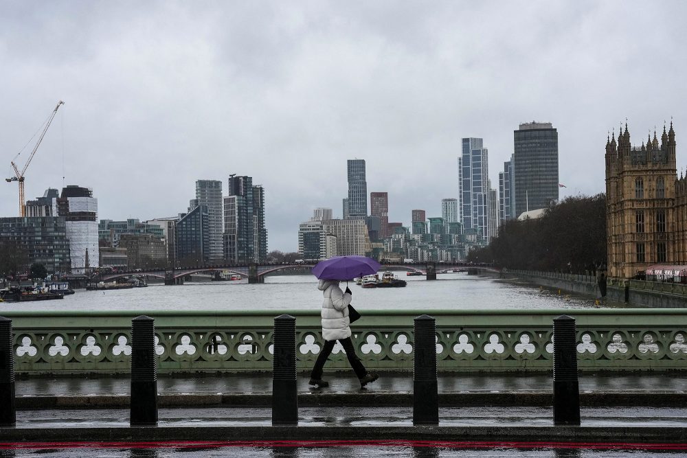 Eine Person geht mit aufgespanntem Regenschirm über die Westminister Bridge in London