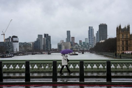 Eine Person geht mit aufgespanntem Regenschirm über die Westminister Bridge in London