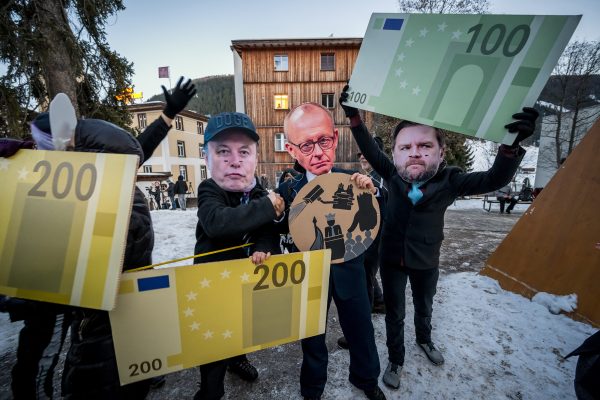 Demonstranten mit Masken von Tesla-CEO Elon Musk, Bundeskanzler Friedrich Merz und US-Vizepräsident JD Vance halten Pappausschnitte von Euro-Banknoten