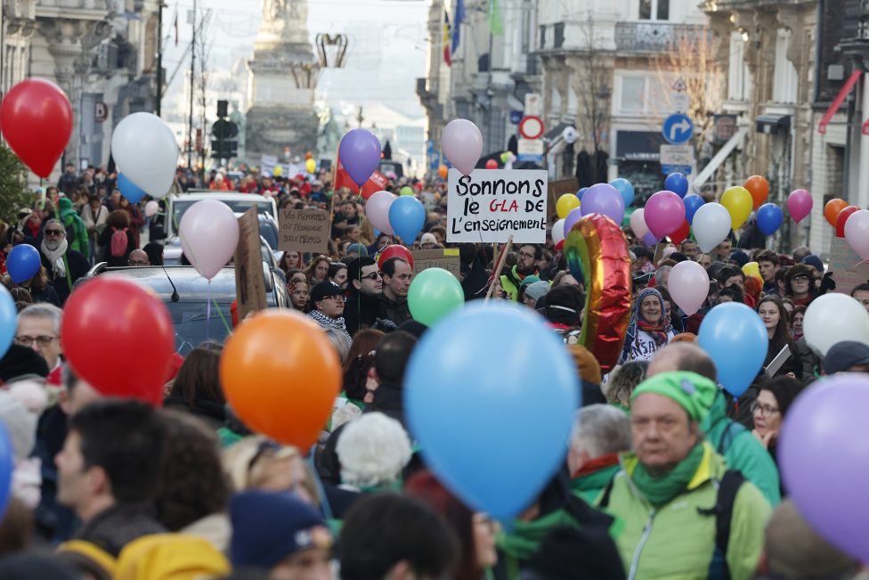 Demonstranten in Brüssel halten bunte Luftballons, außerdem hält ein Demonstrant ein Protestschild hoch