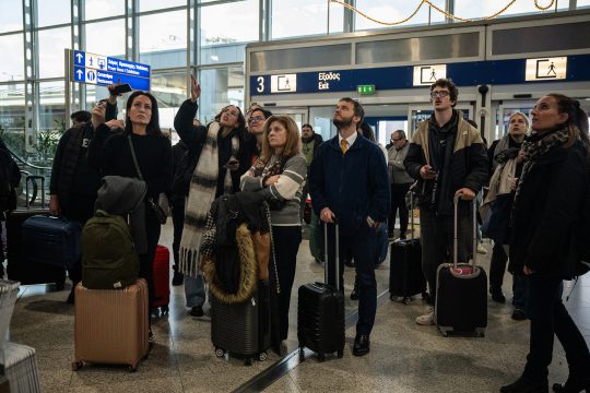 Passagiere am Athener Flughafen schauen auf Tafel mit Fluginformation