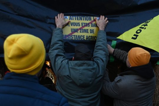 Männer halten ein Schild mit der Aufschrift "Achtung - Sie betreten eine aktive landwirtschaftliche Widerstandszone"