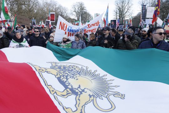 Demonstranten halten eine iranische Flagge, außerdem ist ein Transparent zu sehen