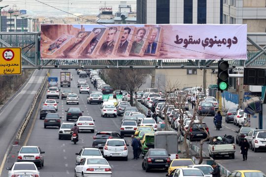 Straßenverkehr in Teheran unter einem Banner mit den Bildern früherer und gegenwärtiger Staatschefs, auf dem auf Farsi "Dominoeffekt" zu lesen ist