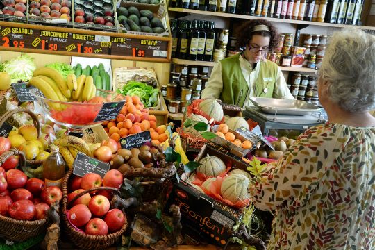 Ladenlokal mit Obst, Wein und Konserven, Verkäuferin bedient Kundin