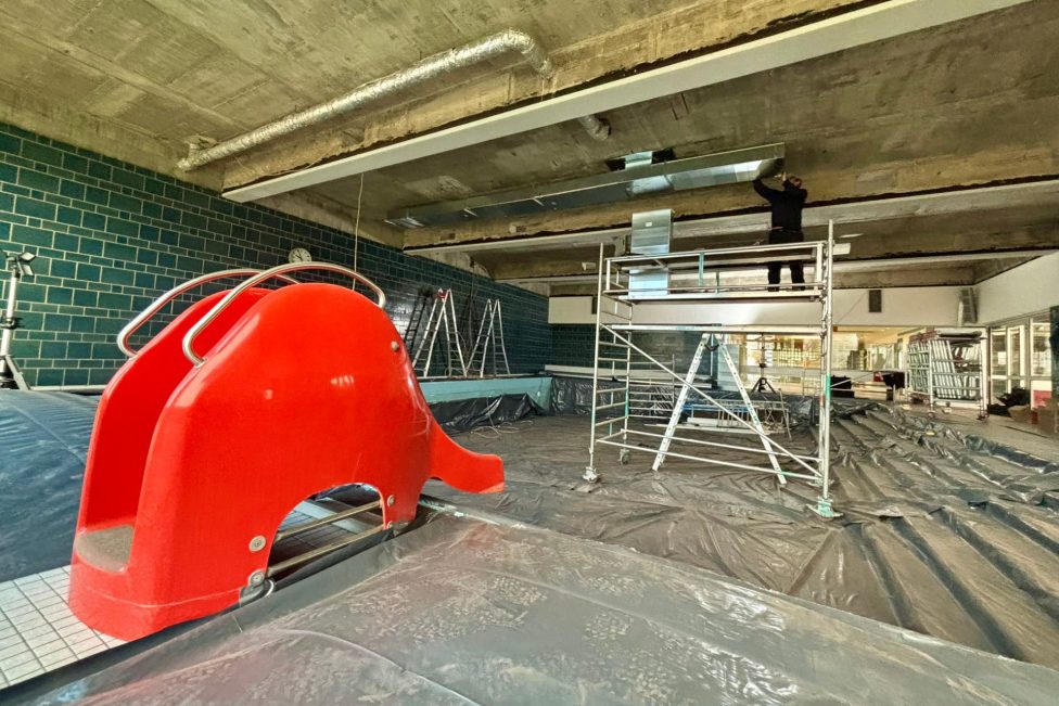 ein Arbeiter auf einem Gerüst arbeitet an der Decke, im Vordergrund eine rote Kinder-Rutschbahn