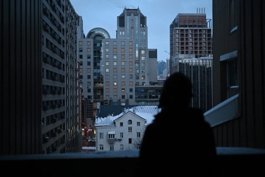 Die 67-jährige ukrainische Künstlerin Oksana Gordiets blickt am 25. Januar 2026 in Kiew von ihrem Balkon auf ein Gebäude, dessen Fenster durch Beschuss zerbrochen sind.