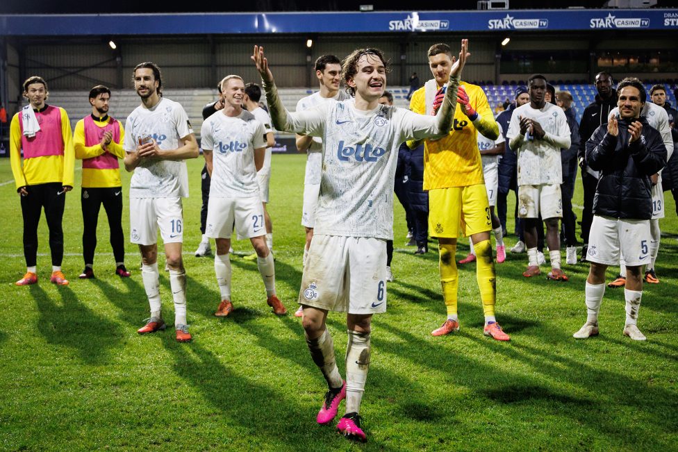 Kamiel Van De Perre lächelt freudestrahlend und hebt die Arme in die Höhe, auch einige Mannschaftskollegen applaudieren im Hintergrund den Fans zu