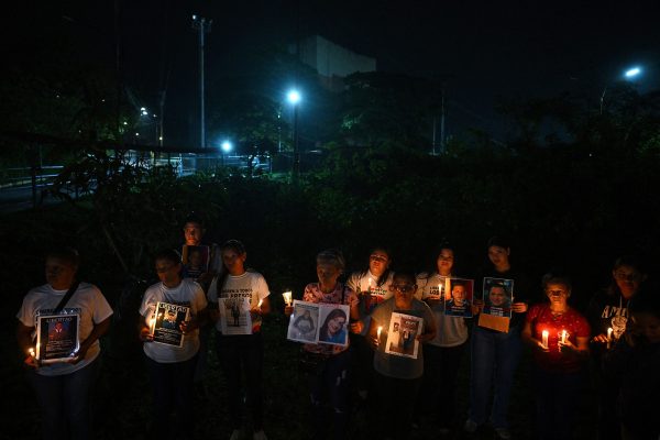 Menschen stehen im Dunkeln vor dem Gefängnis. Sie halten brennende Kerzen und Plakate mit den Bildern inhaftierter Menschen in den Händen