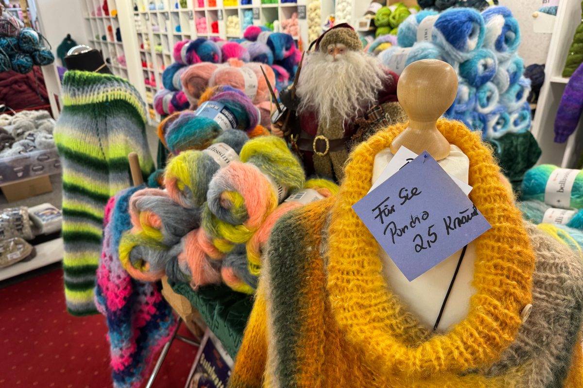Ein gestrickter Poncho auf einer Modepuppe mit einem Hinweis, wie viele Knäuel dafür notwendig sind