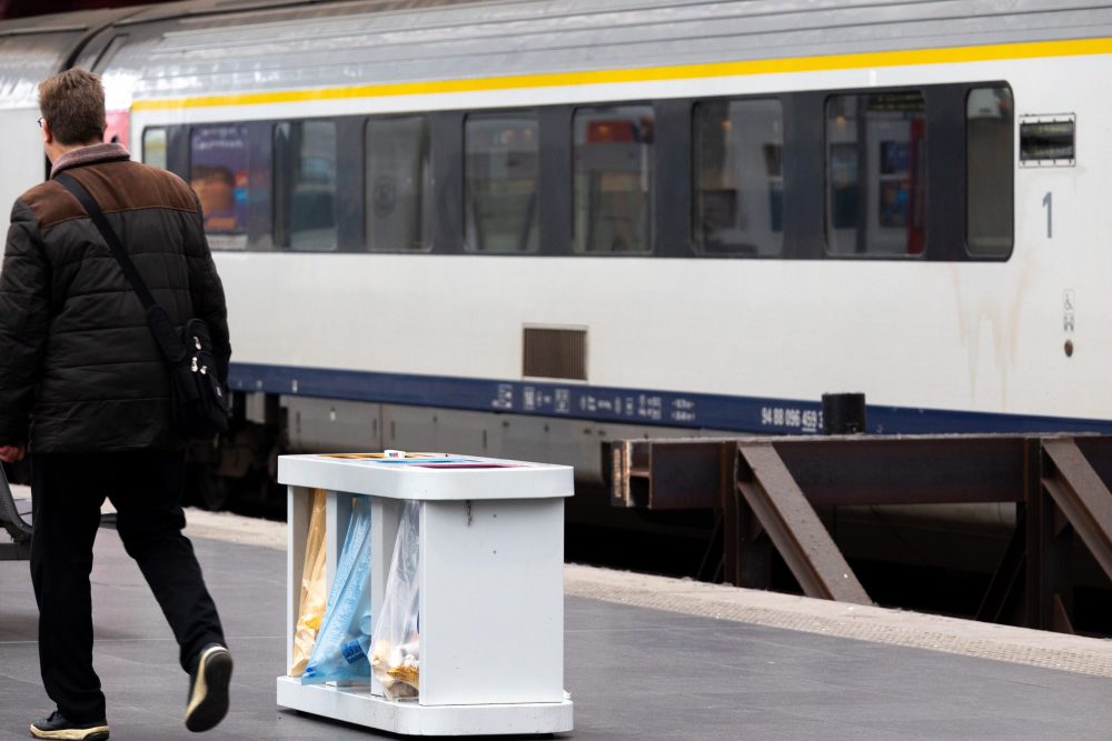 Ein Mann geht auf dem Bahnsteig im Antwerpener Bahnhof an einem haltenden Zug vorbei. Im Vordergrund eien Müllstation mit verschiedenen Mülleimern zum Trennen des Abfalls