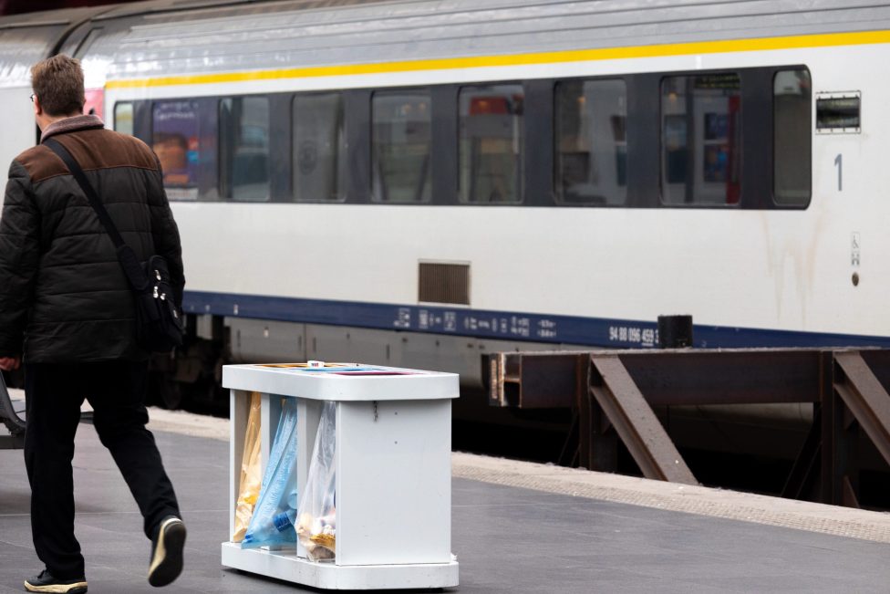 Ein Mann geht auf dem Bahnsteig im Antwerpener Bahnhof an einem haltenden Zug vorbei. Im Vordergrund eien Müllstation mit verschiedenen Mülleimern zum Trennen des Abfalls