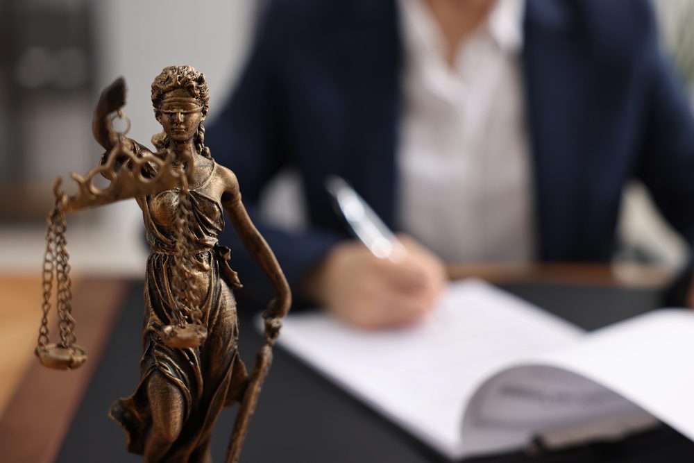 Anwältin notiert auf Papier, auf dem Schreibtisch steht eine Justitia-Statue