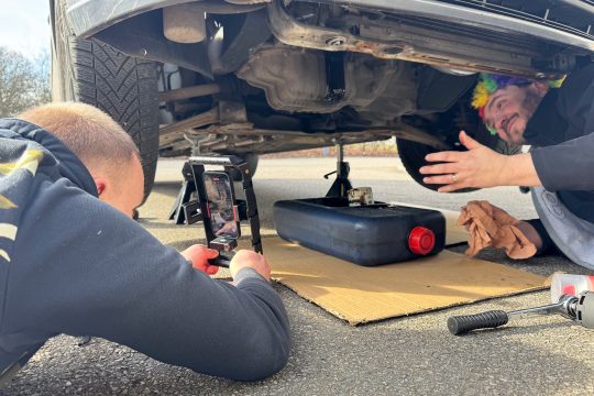 Jean-Marie Dreessens unter dem Auto erklärt, Noah Ernst filmt