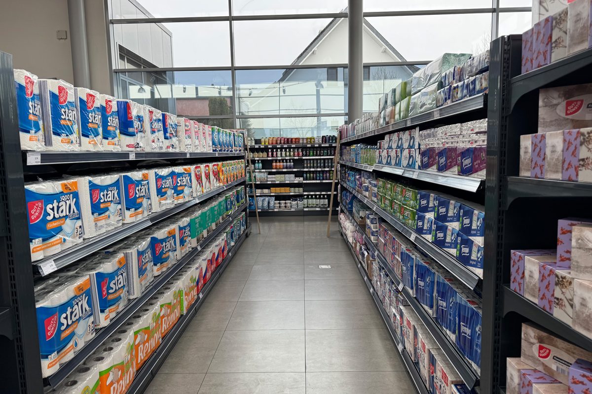 links und rechts Regale mit Toilettenpapier und Papiertaschentüchern, im Hintergrund ein Regal mit Flaschen