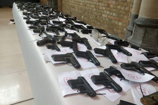 Handfeuerwaffen liegen aufgereiht auf einem Tisch