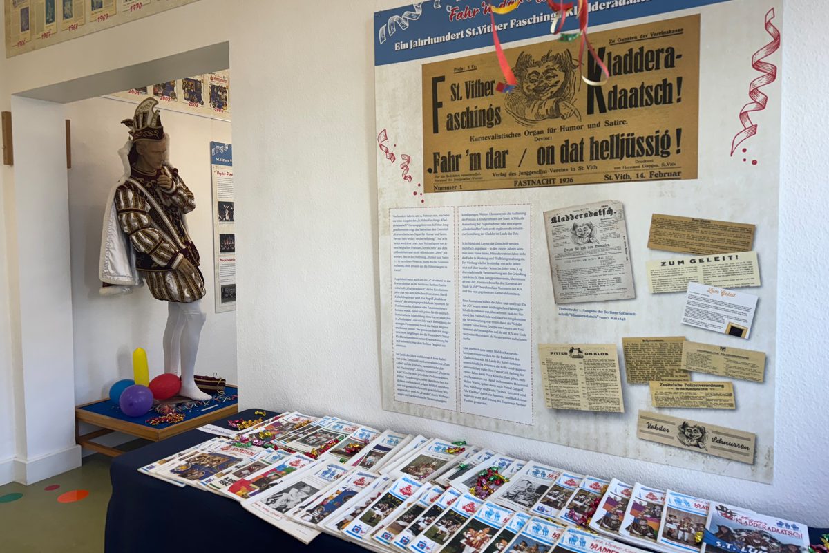 Ausschnitte aus Zeitschriften der verschiedenen Jahre auf einer Schautafel, davor liegen Zeitschriften auf einem Tisch, links ist eine Schaufensterpuppe, die mit einem Karnevalskostüm bekleidet wurde