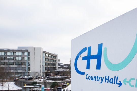 Im Vordergrund ein Hinweisschild mit der Aufschrift CHU, im Hintergrund einer der charakteristischen Türme der Uniklinik CHU