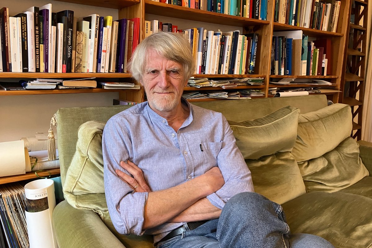 Philippe Van Parijs sitzt auf einem Sofa, im Hintergrund Regale mit Büchern