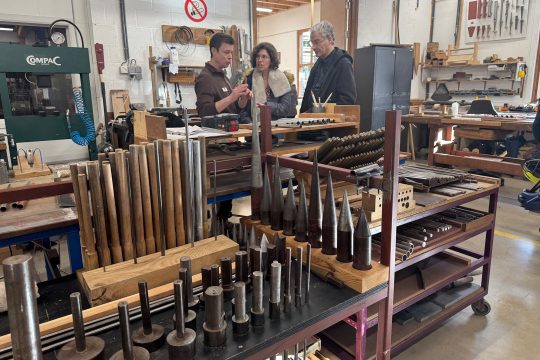 Besucher lassen sich von einem Mitarbeiter etwas erklären, im Vordergrund sind Regale mit Orgelpfeifen