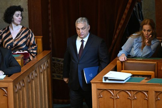 Ungarns Ministerpräsident Viktor Orban betritt den Sitzungssaal, Akten unter dem Arm. Eine Abgeordnete schaut zu ihm, eine andere schaut nach vorn