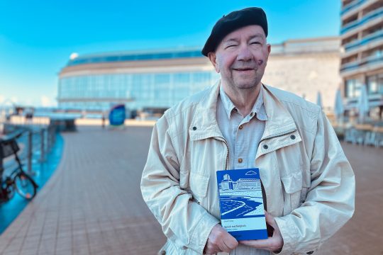 Armin Foxius hält sein Buch in den Händen und lächelt in die Kamera