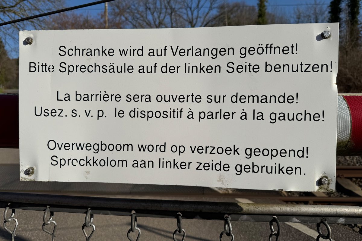 Das Schild erklärt in drei Sprachen, dass sich die Schranke nur auf Anfrage öffnet