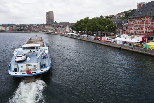 Marktstände entlang des Ufers beim Sonntagsmarkt "La Batte" in Lüttich, davor die Maas, auf der ein Schiff fährt