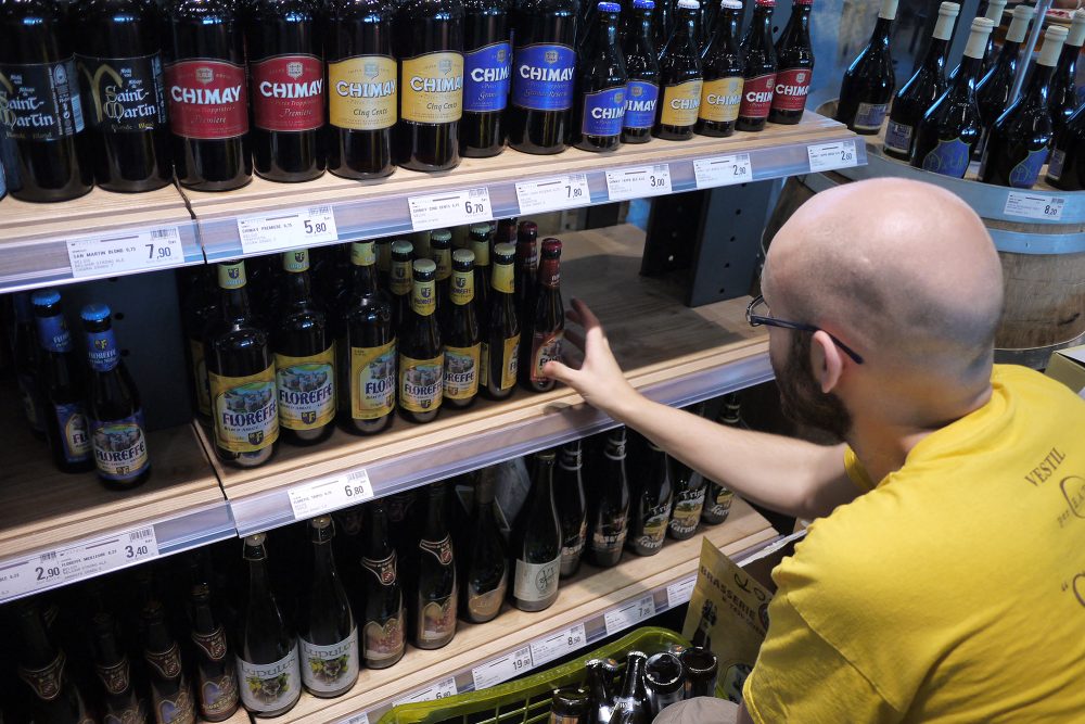 ein Mann hockt im Supermarkt vor einem Regal mit verschiedenen Biersorten