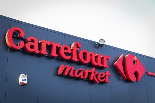 Logo und Schriftzug vor Carrefour an der Außenfassade eines Supermarktes
